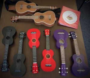 8 ukuleles and binder on desk